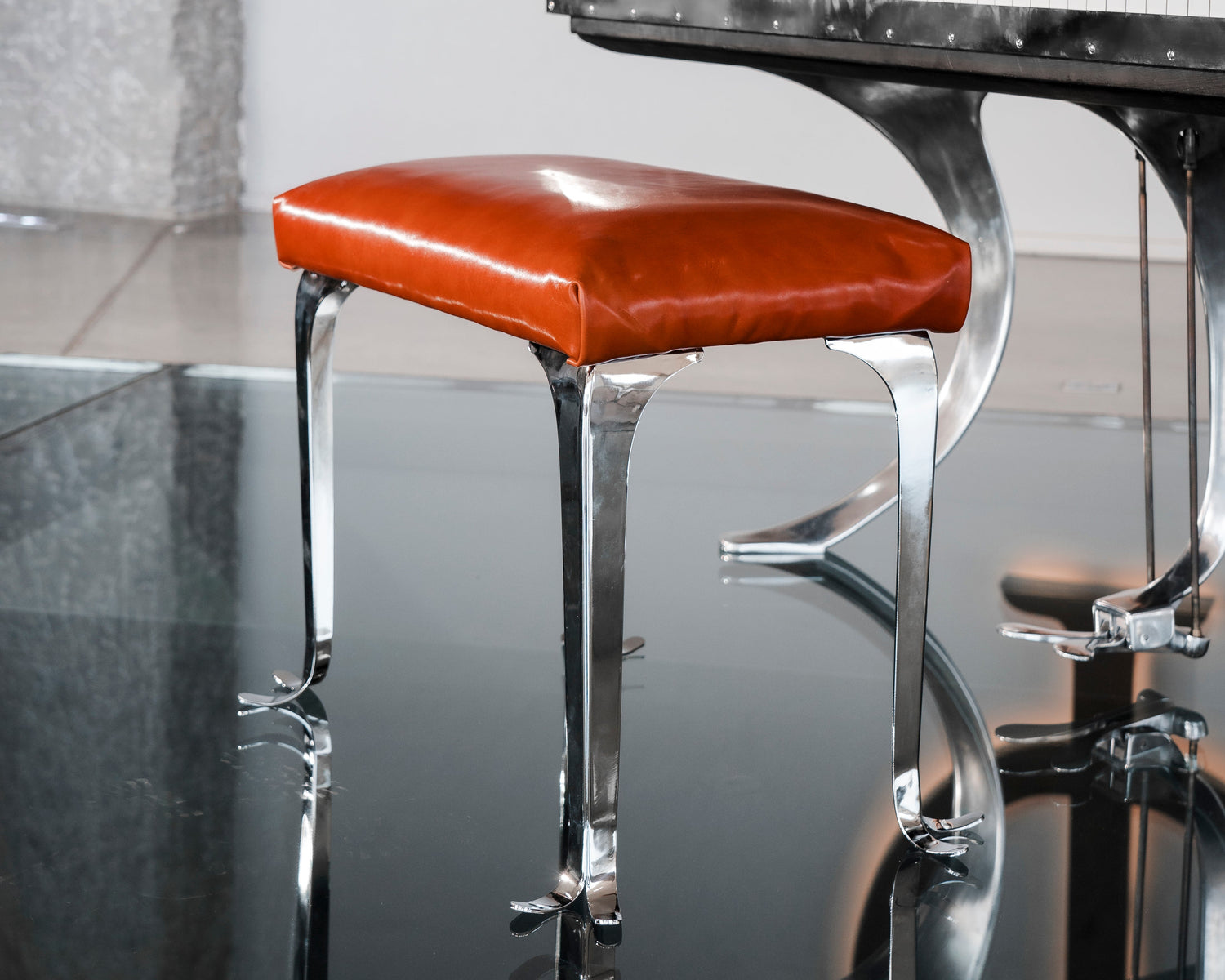 Brown PH piano bench stool with chrome metal legs and walnut color leather seat in front of a piano